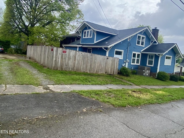 view of side of home featuring a yard, dirt driveway, fence, and a chimney