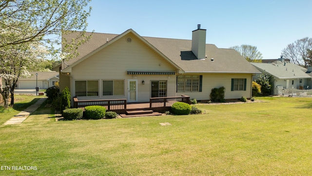 back of house featuring roof with shingles, a chimney, a wooden deck, and a lawn