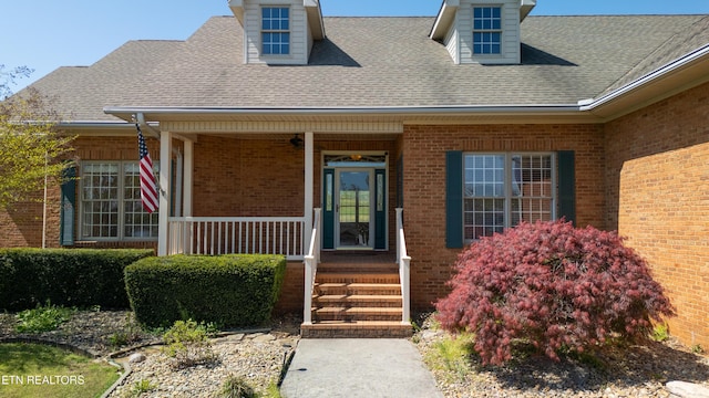 entrance to property with a porch, roof with shingles, and brick siding