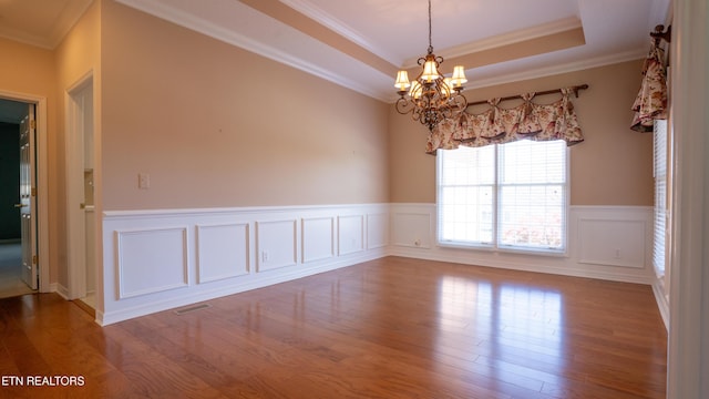 spare room with visible vents, a raised ceiling, an inviting chandelier, wood finished floors, and a wainscoted wall