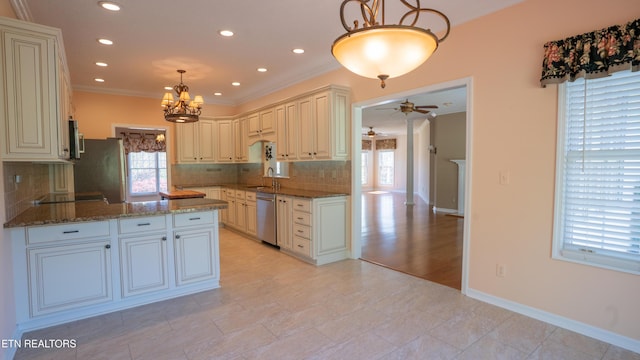 kitchen featuring dark stone counters, ceiling fan with notable chandelier, appliances with stainless steel finishes, a sink, and backsplash
