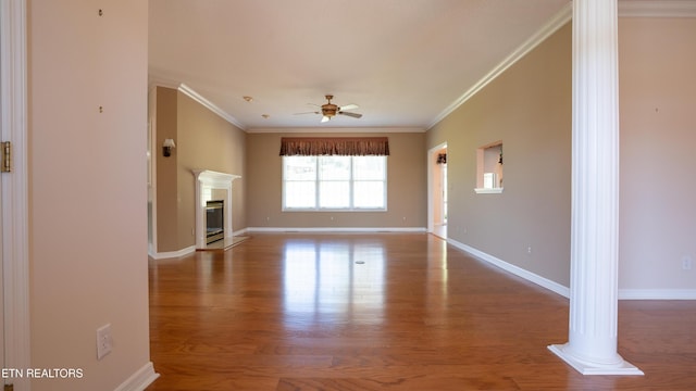 unfurnished living room with a glass covered fireplace, ornamental molding, ornate columns, ceiling fan, and wood finished floors