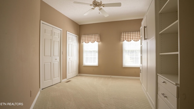 unfurnished bedroom with baseboards, light colored carpet, two closets, and a textured ceiling