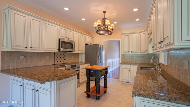 kitchen with an inviting chandelier, ornamental molding, a peninsula, appliances with stainless steel finishes, and a sink