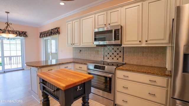 kitchen featuring dark stone countertops, a peninsula, cream cabinetry, decorative backsplash, and stainless steel appliances