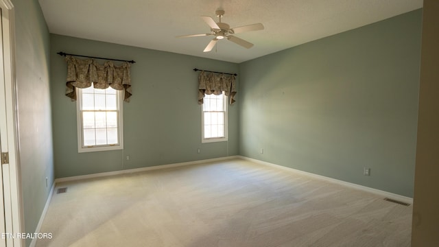 carpeted spare room featuring visible vents, baseboards, and ceiling fan
