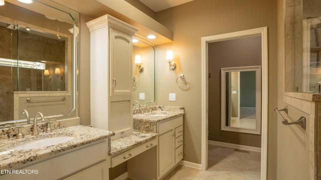 full bathroom featuring a tile shower, two vanities, a sink, and baseboards