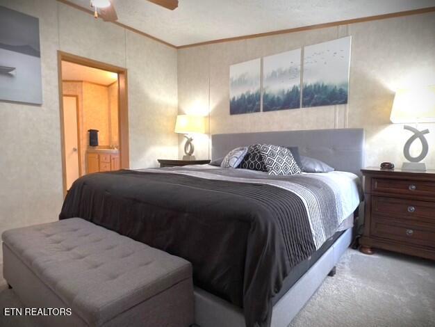 carpeted bedroom featuring crown molding, ensuite bath, and a ceiling fan