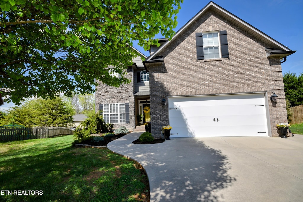 traditional-style house featuring a front yard, fence, brick siding, and driveway