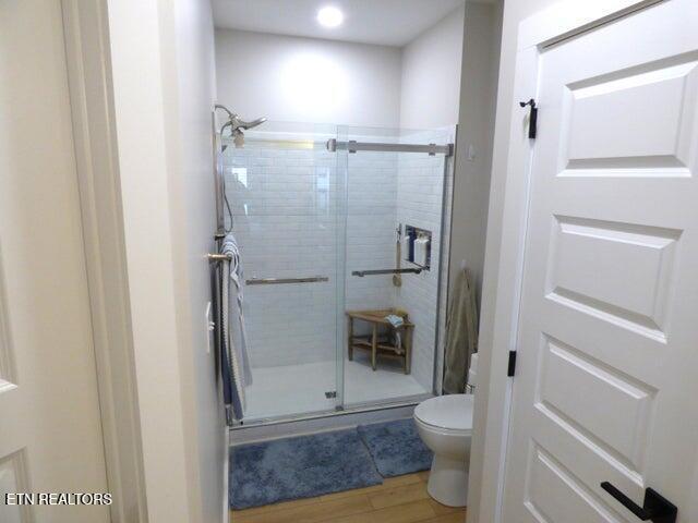 bathroom featuring toilet, wood finished floors, and a shower stall