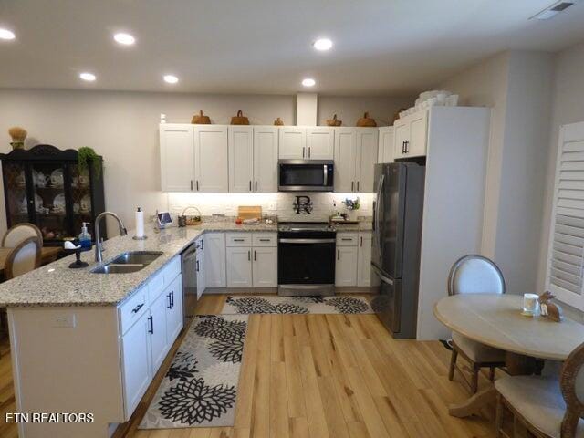 kitchen featuring a sink, light wood-type flooring, a peninsula, stainless steel appliances, and light stone counters