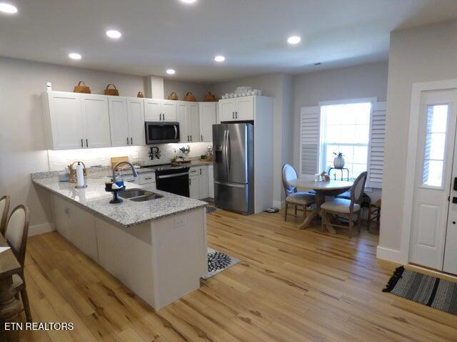 kitchen featuring light wood-style flooring, a peninsula, white cabinets, appliances with stainless steel finishes, and a sink