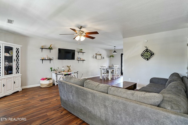 living area featuring visible vents, baseboards, a ceiling fan, a textured ceiling, and dark wood finished floors