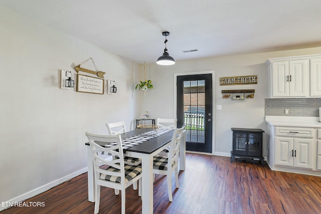 dining space with a wood stove, visible vents, baseboards, and dark wood finished floors