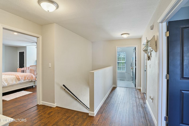 hall featuring baseboards, an upstairs landing, wood finished floors, and a textured ceiling