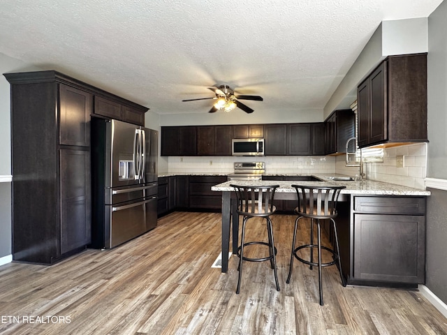 kitchen featuring appliances with stainless steel finishes, a peninsula, light wood-style floors, ceiling fan, and a sink
