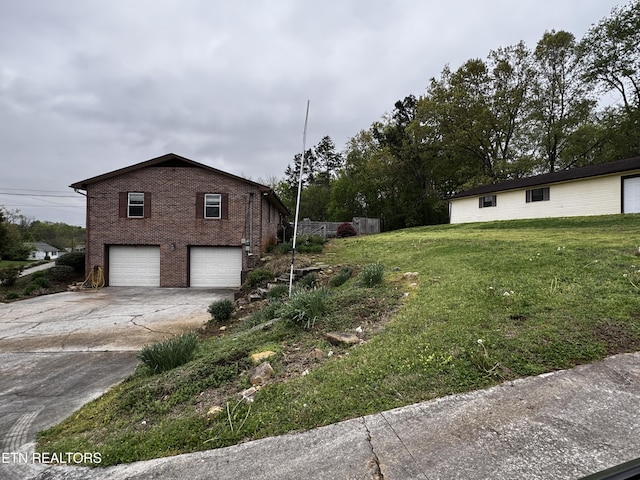 view of property exterior featuring an attached garage, a yard, driveway, and brick siding