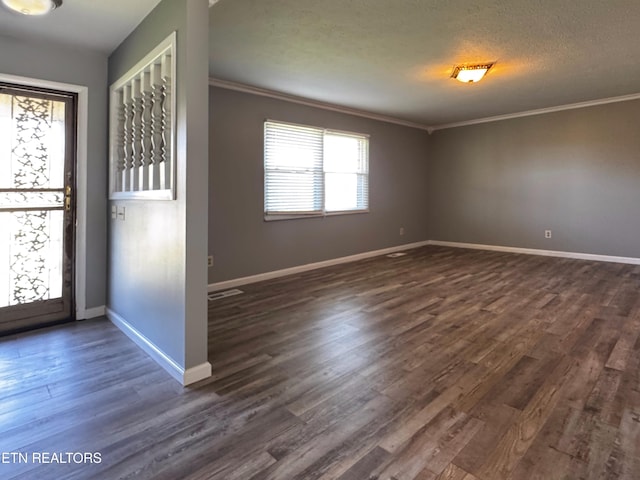 empty room featuring dark wood-type flooring, visible vents, baseboards, and crown molding