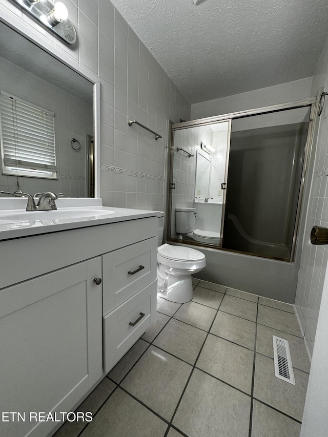 bathroom featuring shower / bath combination with glass door, tile patterned flooring, visible vents, toilet, and tile walls