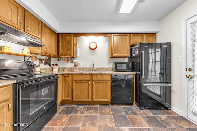 kitchen with a sink, stone finish floor, under cabinet range hood, black appliances, and light stone counters
