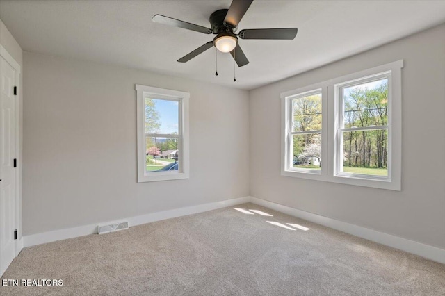 carpeted spare room with visible vents, baseboards, and ceiling fan