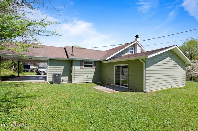 rear view of house featuring a yard, a carport, central AC, and a chimney