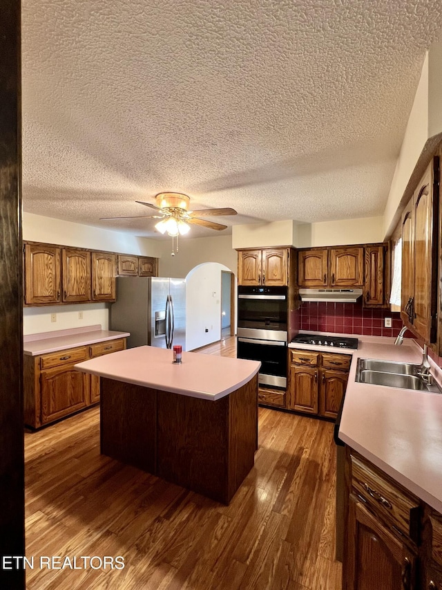 kitchen featuring under cabinet range hood, a textured ceiling, a sink, and appliances with stainless steel finishes