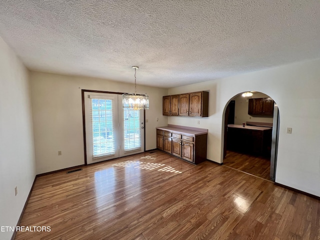 unfurnished dining area with arched walkways, wood finished floors, an inviting chandelier, and a textured ceiling