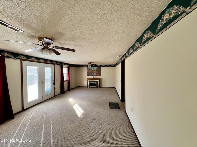 unfurnished living room with a textured ceiling, light colored carpet, a ceiling fan, and visible vents