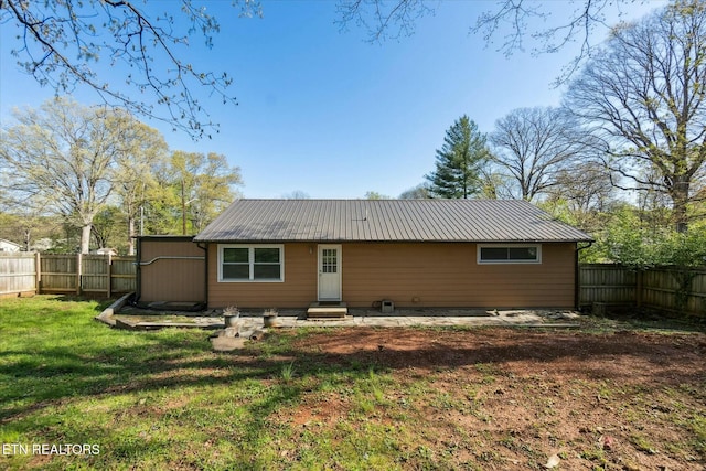 rear view of house featuring entry steps, metal roof, and a fenced backyard
