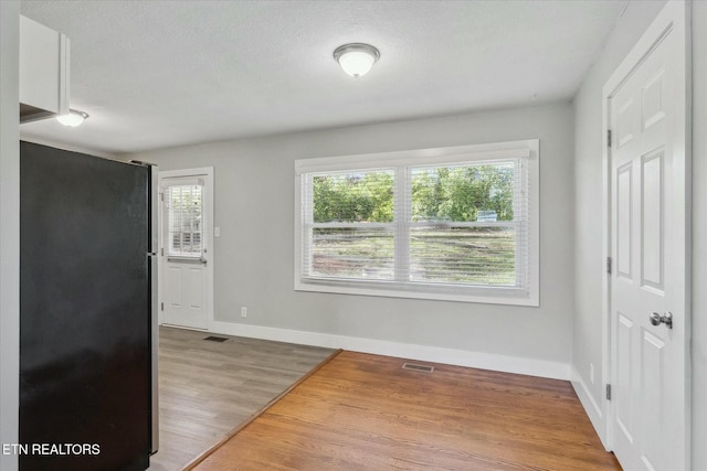 interior space with a textured ceiling, wood finished floors, baseboards, and visible vents