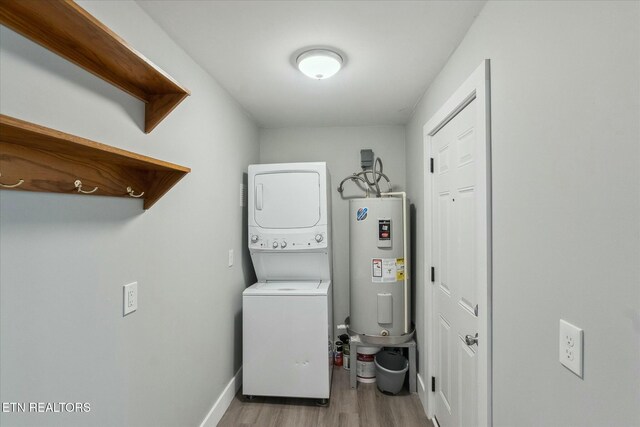 laundry room featuring baseboards, laundry area, stacked washer and dryer, wood finished floors, and water heater