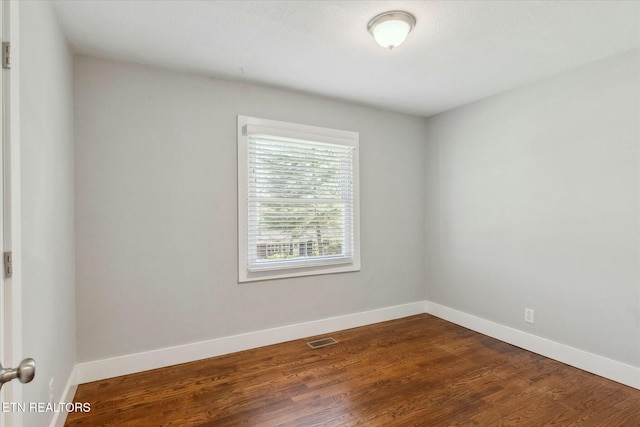 empty room featuring visible vents, baseboards, and dark wood finished floors