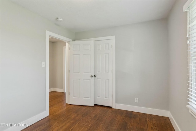 unfurnished bedroom featuring a closet, baseboards, multiple windows, and dark wood finished floors