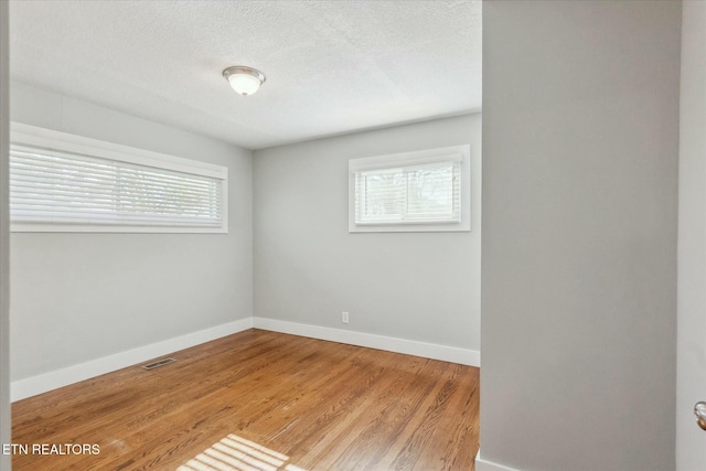 empty room featuring visible vents, baseboards, wood finished floors, and a textured ceiling