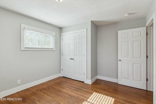 unfurnished bedroom with a textured ceiling, wood finished floors, baseboards, and a closet