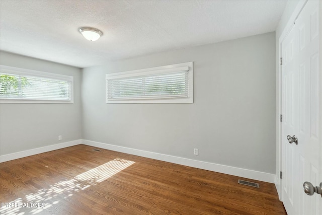 empty room featuring visible vents, baseboards, a textured ceiling, and wood finished floors