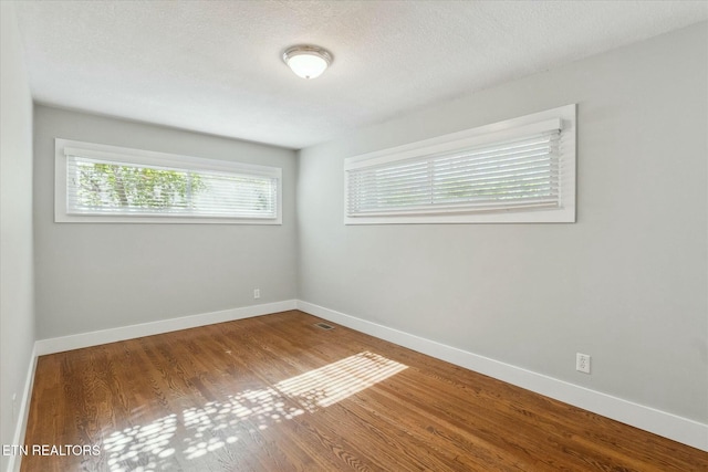 empty room featuring baseboards, a textured ceiling, and wood finished floors