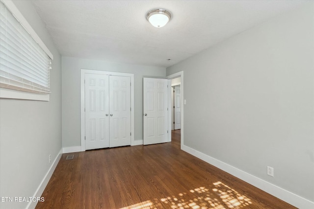 unfurnished bedroom with visible vents, a closet, baseboards, and wood finished floors