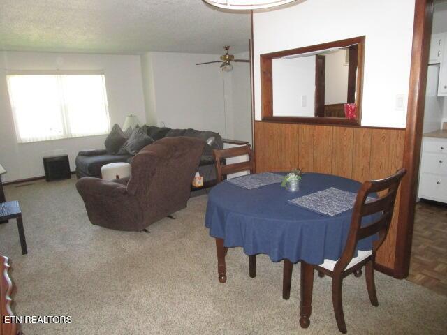 carpeted dining room with wood walls and a ceiling fan