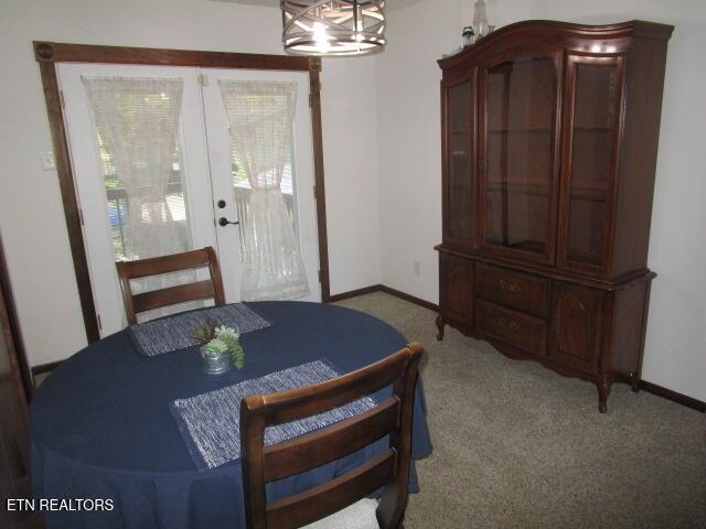 carpeted dining space with a notable chandelier, baseboards, and french doors
