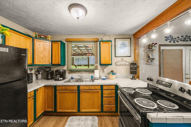 kitchen featuring freestanding refrigerator, electric range, a textured ceiling, a sink, and light wood finished floors