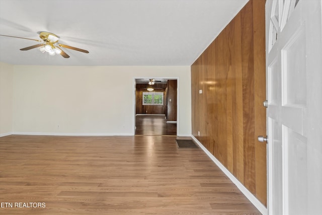 empty room featuring light wood finished floors, wooden walls, a ceiling fan, and baseboards