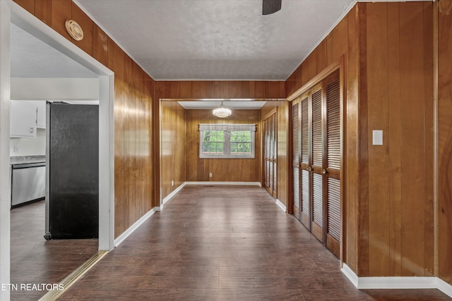 hall with a textured ceiling, wood finished floors, wood walls, and baseboards