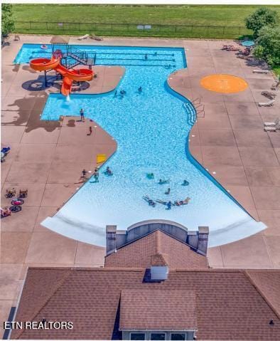 pool featuring a water play area, a water slide, fence, and a patio area