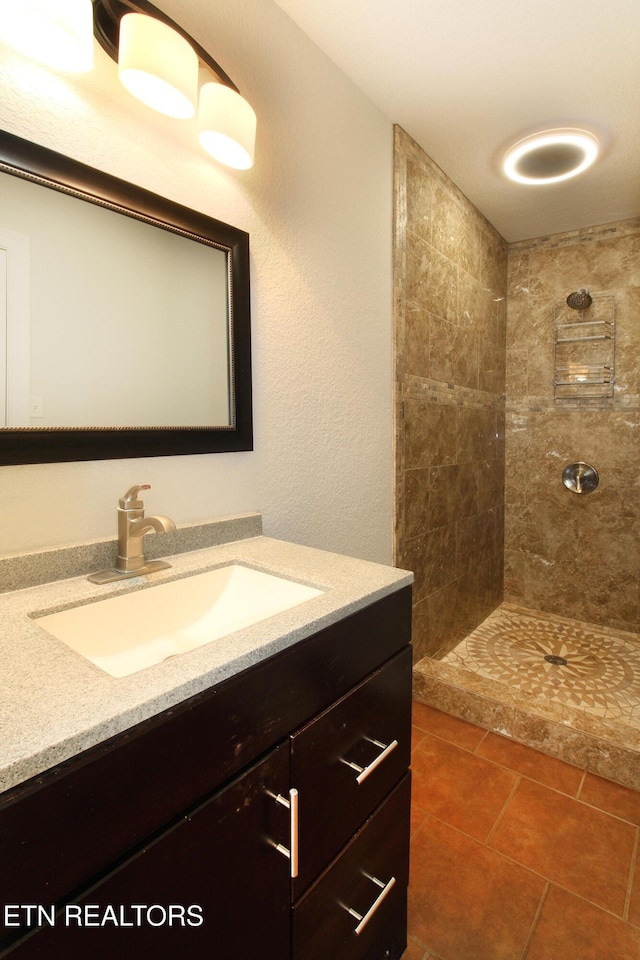 bathroom featuring tile patterned flooring, a tile shower, and vanity