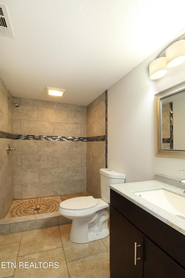 bathroom featuring visible vents, a tile shower, toilet, a textured wall, and vanity
