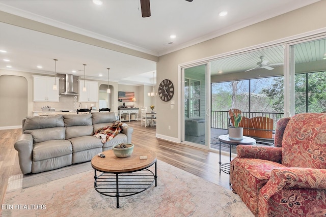 living area featuring ornamental molding, ceiling fan, light wood-type flooring, and baseboards