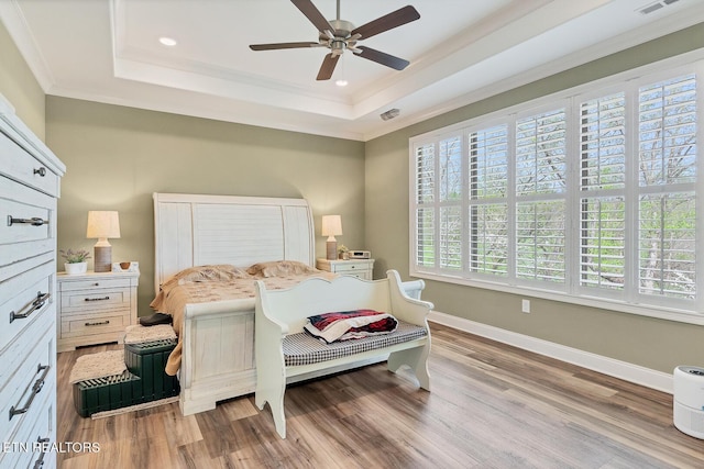 bedroom featuring a tray ceiling, baseboards, ornamental molding, and light wood-style flooring