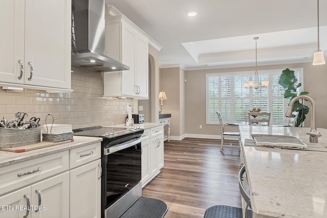 kitchen with wall chimney range hood, crown molding, a tray ceiling, stainless steel electric range, and decorative backsplash